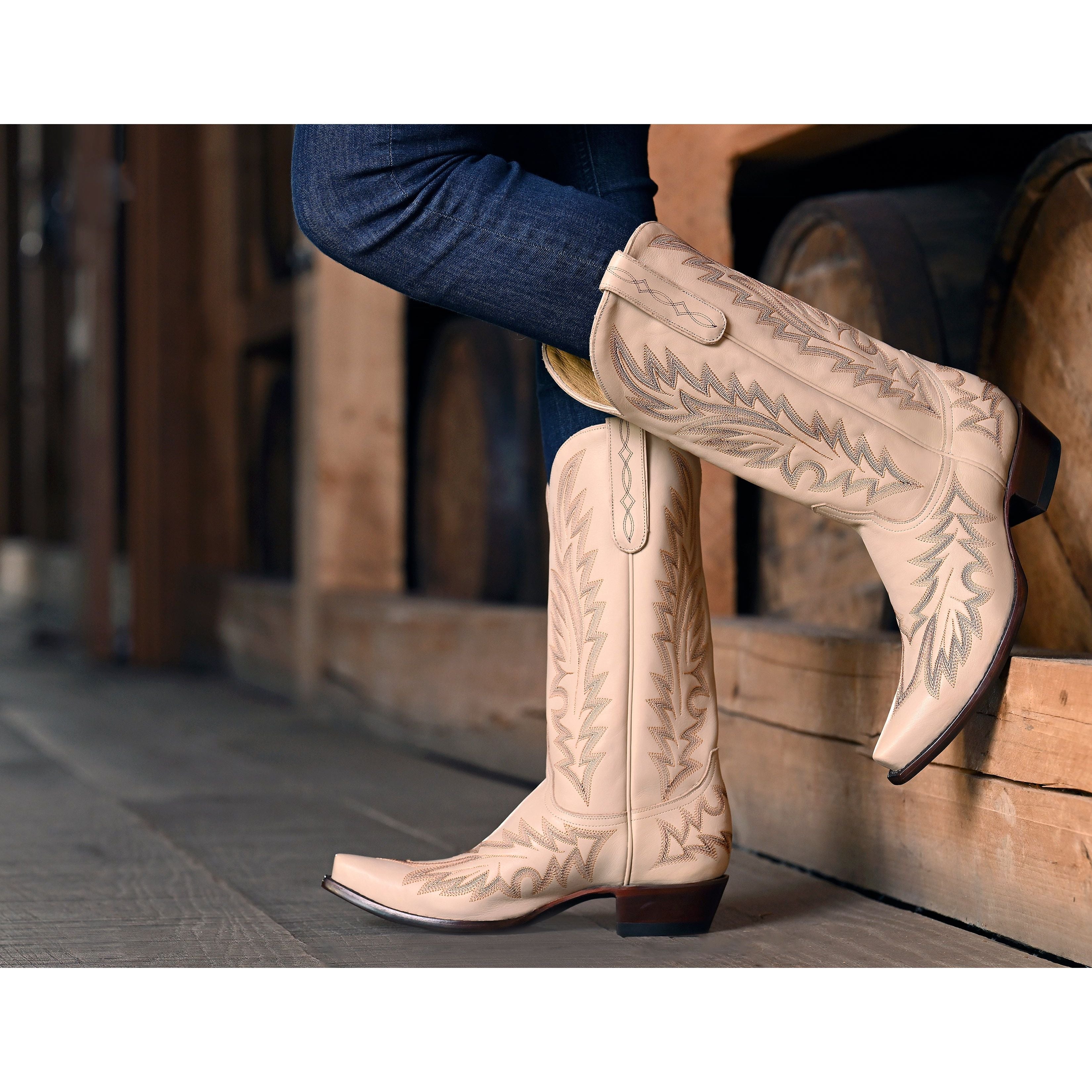 Beige cowboy boots with intricate designs worn by a person sitting on wooden steps.